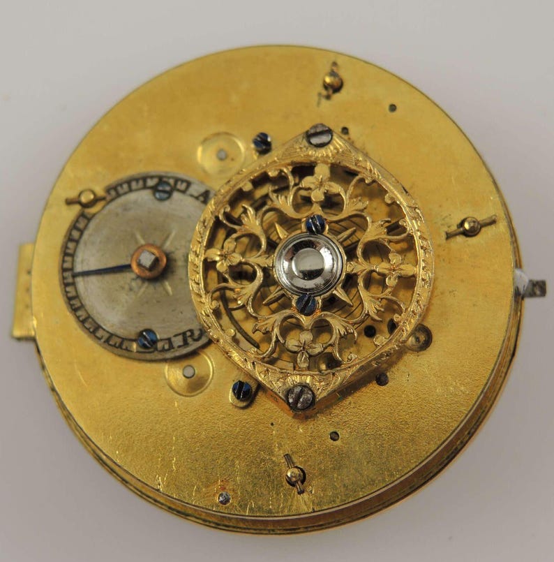 Puede incluir: Un reloj de bolsillo dorado con un dise&ntilde;o calado decorativo. La esfera del reloj es visible y tiene una sola aguja.