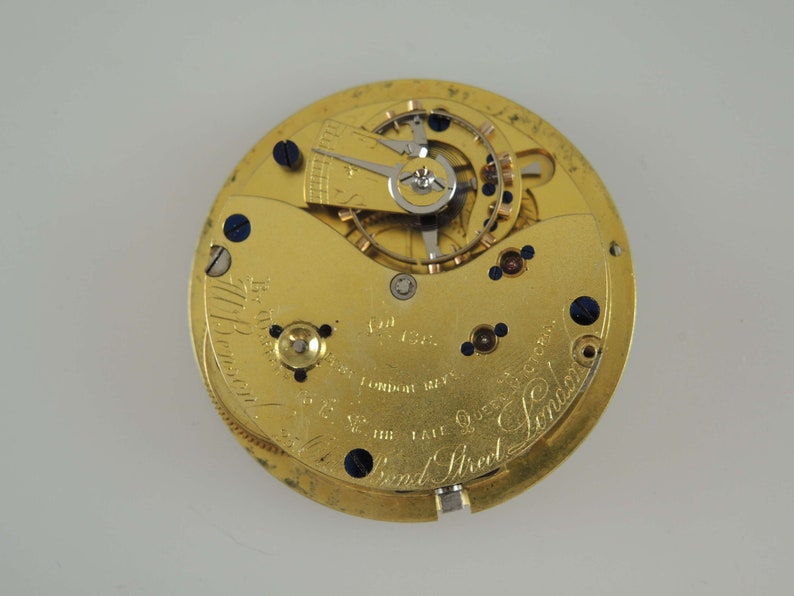 Op de afbeelding: Een close-up van een goudkleurig uurwerk met ingewikkelde tandwielen, schroeven en een balanswiel. Het uurwerk heeft tekst die luidt "178 Bond Street London". Dit is een vintage horloge.