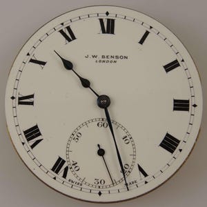 Puede incluir: Una esfera de reloj de bolsillo blanca con marcadores de hora en n&uacute;meros romanos negros y agujas negras. La esfera del reloj tambi&eacute;n tiene un c&iacute;rculo conc&eacute;ntrico m&aacute;s peque&ntilde;o con marcas negras para los segundos. La esfera del reloj est&aacute; etiquetada como "J.W. Benson London" y "Swiss Made".