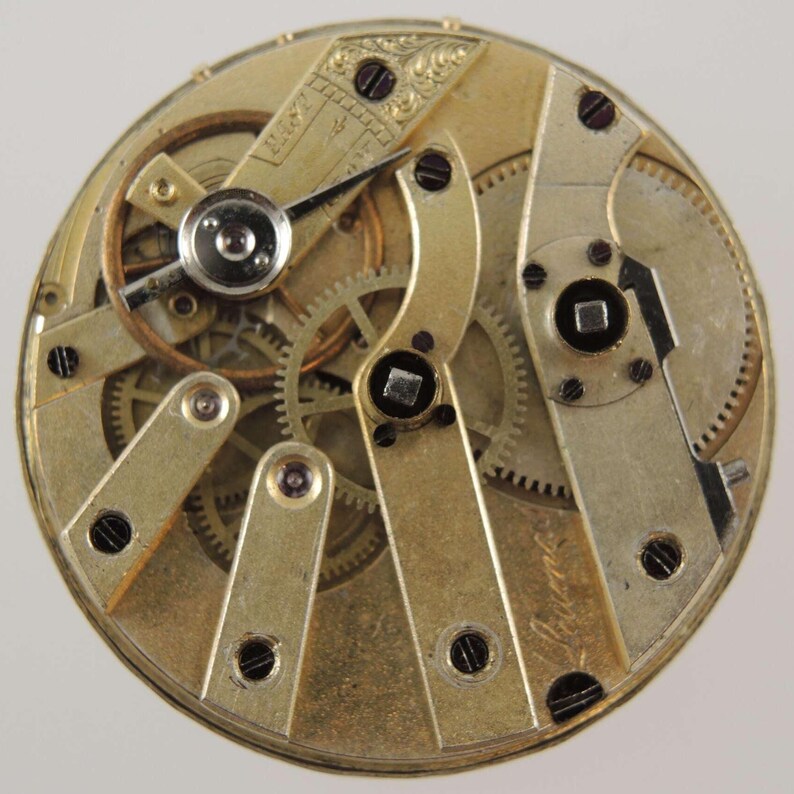 May include: Detailed view of a vintage watch movement. The intricate mechanism features gold-toned gears, levers, and screws. The watch components are arranged in a circular pattern, showcasing the precision of the internal workings.