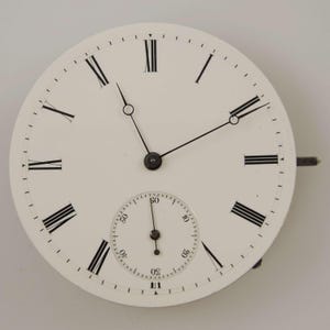 May include: A vintage watch face with a white background, black Roman numerals, and black hands. A smaller dial is at the bottom. The watch face has a metal stem on the right side.