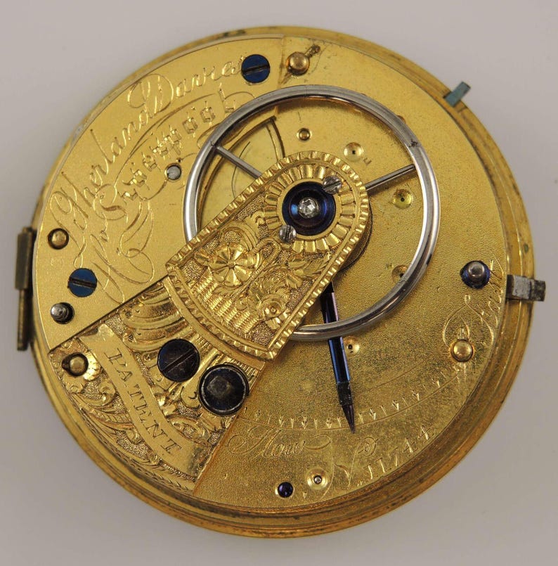 May include: A gold pocket watch with intricate engravings and a visible movement. The watch face is inscribed with "Thomas Darracott London".