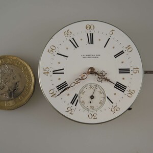 May include: A white pocket watch face with black Roman numeral hour markers and gold Arabic numeral minute markers. The watch face has a smaller, circular sub-dial with black markings and a gold hand. The watch face is signed "G.R. Smith & Son, Philadelphia."