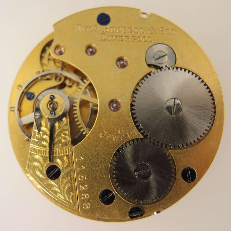 May include: Close-up of a vintage watch movement with intricate gears and components. The gold-toned plate features engraved text and the inscription "Fred. Nussen & Son, Liverpool." The watch mechanism includes 16 jewels and the serial number 115288.