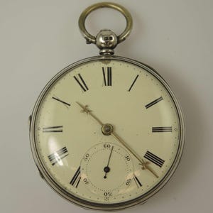 Könnte beinhalten: Eine silberne Taschenuhr mit römischen Ziffern für die Stunden und einem weißen Zifferblatt. Die Uhr hat einen goldenen Sekundenzeiger und ein kleines Zifferblatt für die Sekunden.