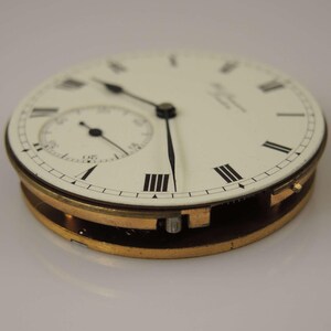 May include: A close-up of a white pocket watch face with black Roman numeral hour markers and black hands. The watch has a gold-toned case and a small seconds dial at the 12 o'clock position.