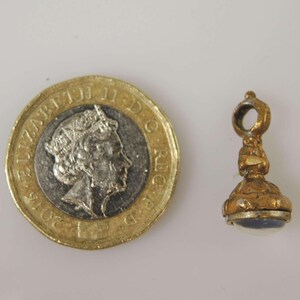 May include: A gold-toned seal with a blue stone set in the top. The seal is about the size of a US one pound coin.