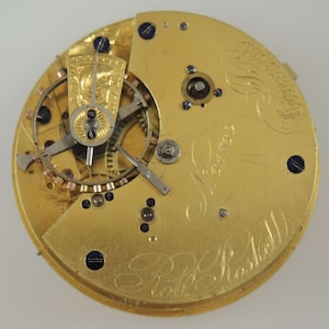 May include: Close-up of the inner workings of a gold pocket watch with the inscription "J. Lawson, Watchmaker, Bristol" on the face.