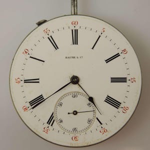 Puede incluir: Una esfera de reloj de bolsillo blanca con marcadores de hora en n&uacute;meros romanos negros y marcadores de minutos negros. La esfera del reloj tiene un subdial blanco m&aacute;s peque&ntilde;o con marcadores de minutos negros. La esfera del reloj est&aacute; firmada con "BAUME & C".
