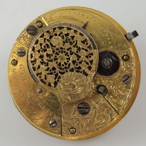 Op de afbeelding: Een gouden zakhorloge met ingewikkelde bloemmotieven en een gedetailleerd gezicht met Romeinse cijfers. Het horloge heeft een klein, rond, open gebied in het midden met een decoratief ontwerp.
