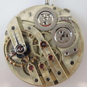 Puede incluir: Una vista cercana del funcionamiento interno de un reloj de bolsillo de plata. El reloj est&aacute; etiquetado como "BADMUS & CO. LONDON" y "Diplome d'Honneur 1881".