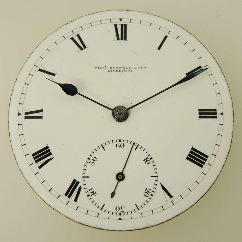 May include: A vintage pocket watch face with a white background, black Roman numerals, and black hands. The watch face has a smaller subdial at the bottom and the text "THOS. RUSSELL & SON LIVERPOOL" is printed at the top.