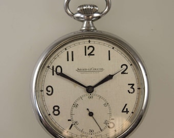 Puede incluir: Un reloj de bolsillo plateado con una esfera blanca y agujas negras. El reloj tiene un pequeño dial de segundero en la parte inferior. La esfera del reloj dice "JAEGER-LECOULTRE FABRIQUE EN SUISSE".