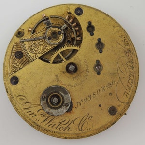 May include: Close-up of the inner workings of a gold pocket watch with the inscription "Wm. Watch Co." and the serial number "N.19380246".