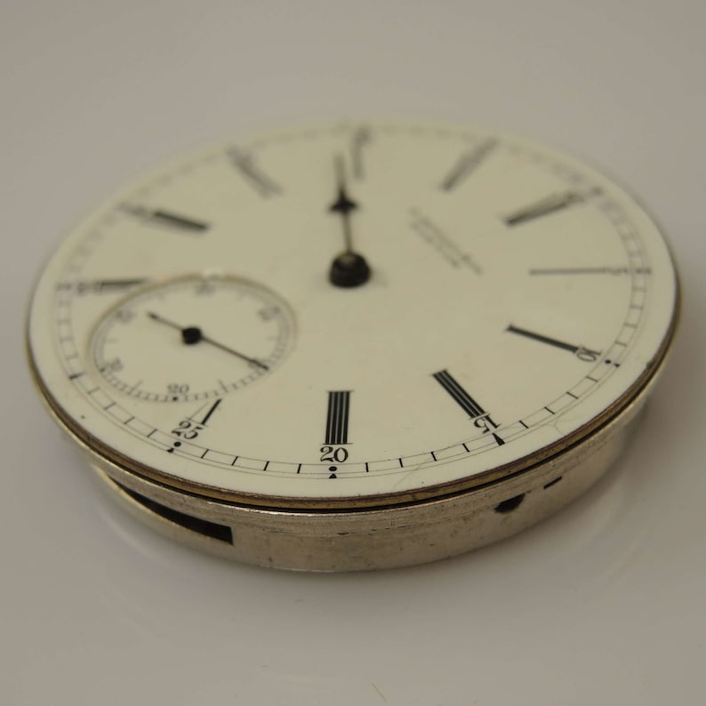 K&ouml;nnte beinhalten: Eine silberne Taschenuhr mit wei&szlig;em Zifferblatt und schwarzen Zeigern. Die Uhr hat ein kleines Hilfszifferblatt bei 12 Uhr.