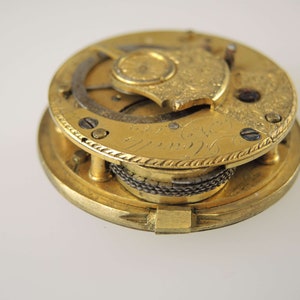 May include: A gold-toned pocket watch movement with intricate engravings and a visible winding mechanism.