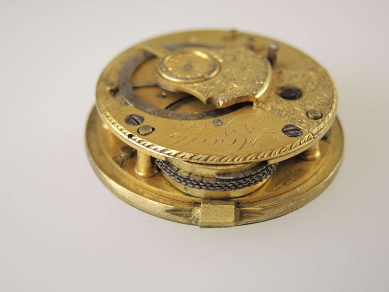 May include: A gold-toned pocket watch movement with intricate engravings and a visible winding mechanism.