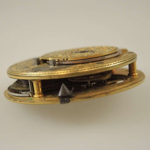 Puede incluir: Un reloj de bolsillo dorado con engranajes intrincados y un dise&ntilde;o circular. El reloj est&aacute; abierto y el mecanismo interno es visible.