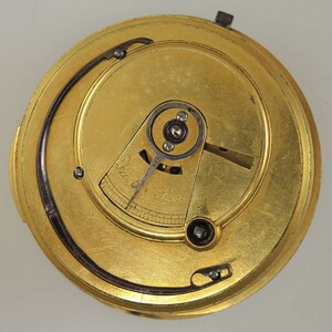 Puede incluir: Primer plano de un movimiento de reloj de color dorado con un mecanismo de cuerda y el texto "Fast 1 Hour" en la esfera.