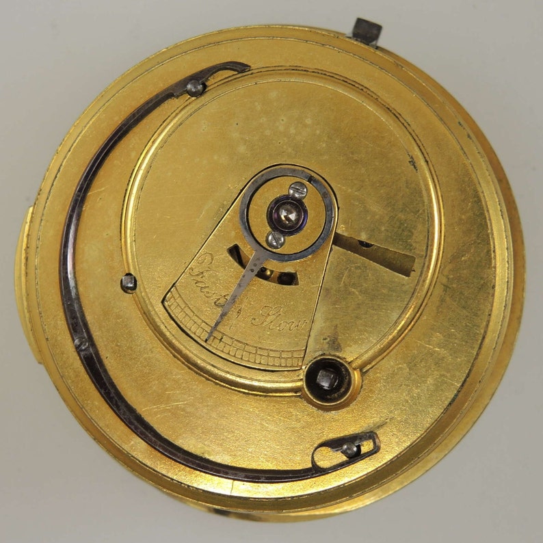 Puede incluir: Primer plano de un movimiento de reloj de color dorado con un mecanismo de cuerda y el texto "Fast 1 Hour" en la esfera.