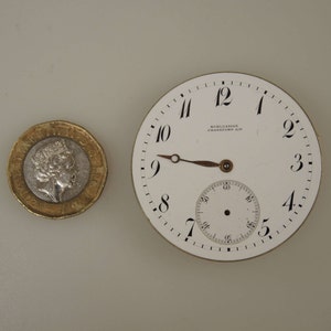May include: A white pocket watch face with black Roman numeral hour markers and black minute markers. The watch face has a small, white sub-dial with black minute markers. The watch face also has the text "SCHLESICKY FRANKFURT AM" printed on it.