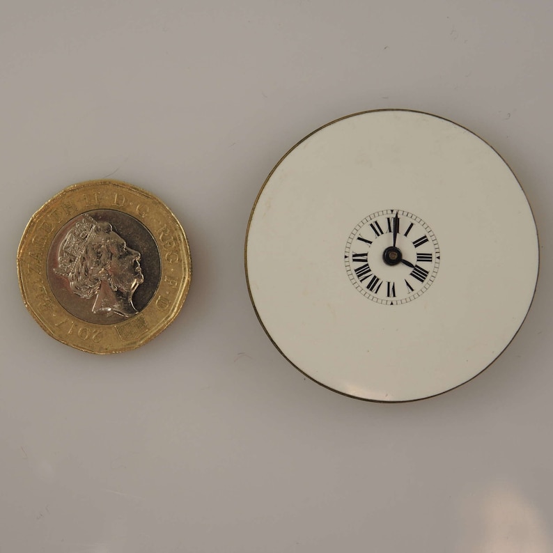 May include: A white porcelain clock face with black Roman numeral hour markers and black hands. The clock face is mounted on a white circular base.