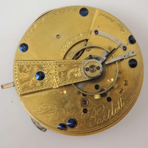May include: Close-up of a gold pocket watch movement with the inscription "E.B. Bartlett" and the number "4996007".