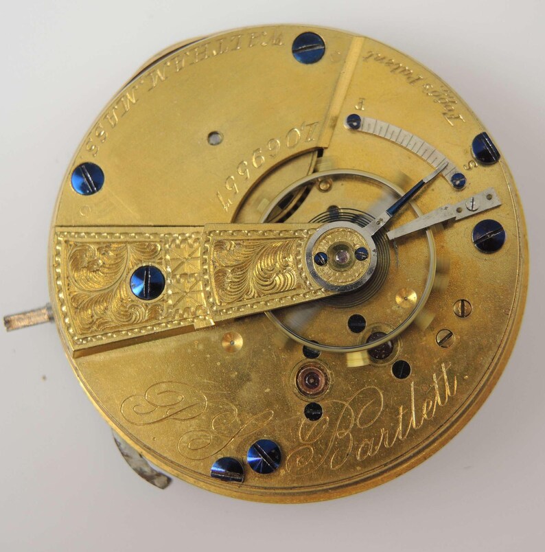 May include: Close-up of a gold pocket watch movement with the inscription "E.B. Bartlett" and the number "4996007".
