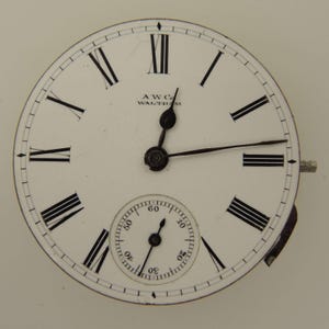 May include: A white pocket watch face with black Roman numerals and hands. The watch face has a smaller subdial at the bottom and the text "AWC Co. WALTHAM" is printed at the top.