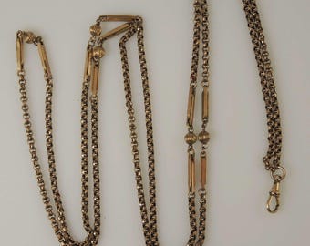May include: A gold chain necklace with a double chain design and decorative accents. The chain has two round beads and four rectangular bars.