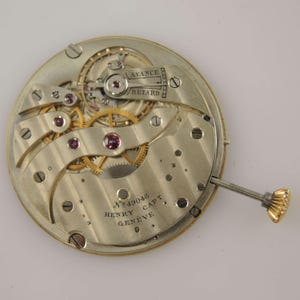 May include: Detailed view of a vintage watch mechanism, showcasing gears, jewels, and metal parts. The watch movement features the text "AVANCE RETARD" and "No 49048 HENRY CAPT GENEVE" engraved on the metal.