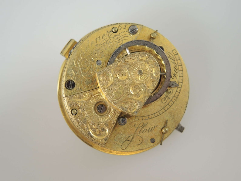K&ouml;nnte beinhalten: Eine goldene Taschenuhr mit aufwendigen Gravuren und einem detaillierten Mechanismus. Das Zifferblatt der Uhr ist mit "J. Flower" und "Chas. Jenner" signiert.