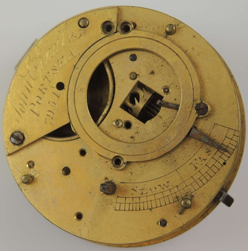 May include: A gold-toned pocket watch movement with the inscription "John Smith & Co. Portsea 7951" visible on the face. The movement has a circular dial with a scale labeled "Slow" and "Fast".