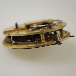 Puede incluir: Primer plano de un movimiento de reloj de bolsillo dorado con engranajes intrincados y un v&aacute;stago de cuerda plateado.