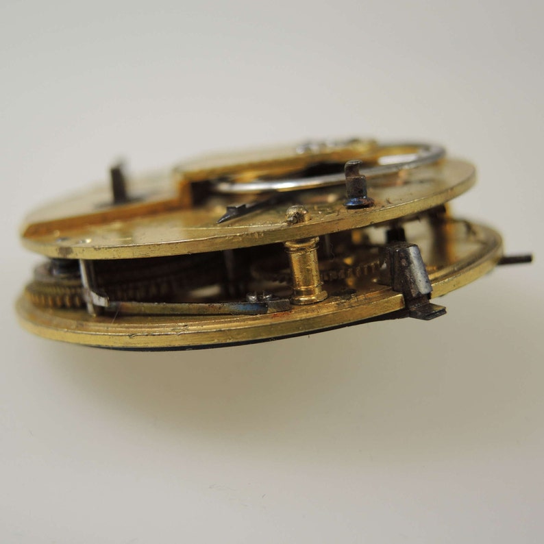 Puede incluir: Primer plano de un movimiento de reloj de bolsillo dorado con engranajes intrincados y un v&aacute;stago de cuerda plateado.