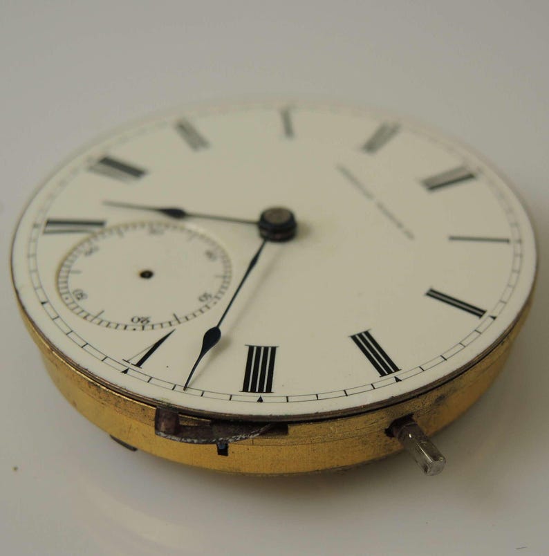 May include: A white pocket watch face with black Roman numeral hour markers and black hands. The watch has a small, white sub-dial with black markings.