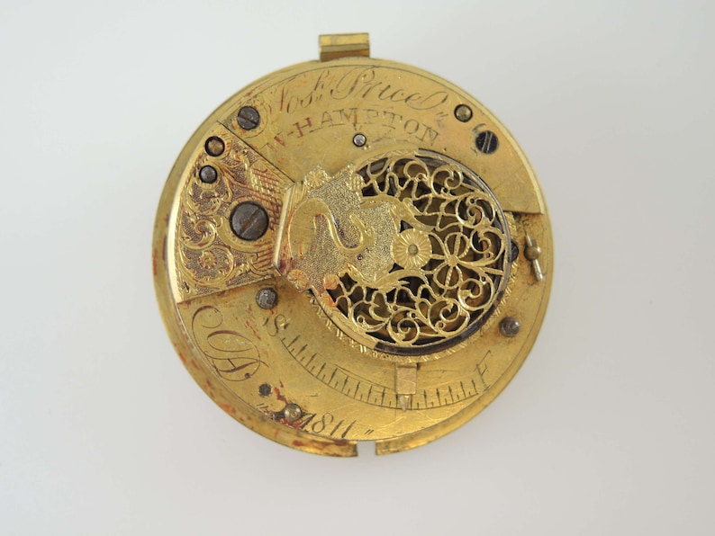 K&ouml;nnte beinhalten: Nahaufnahme eines Vintage-Taschenuhrwerks aus Gold. Der Uhrenmechanismus weist aufwendige Details auf, darunter eingravierte Muster, Zahnr&auml;der und die Inschrift "Nosh Price & W-Hampton". Das Datum "1811" ist ebenfalls sichtbar.
