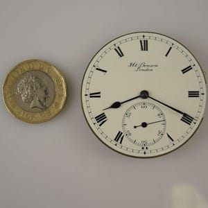 May include: A white pocket watch with black Roman numeral hour markers and black hands. The watch face has the text "J.W. Benson London" printed on it. The watch is about the size of a British one pound coin.