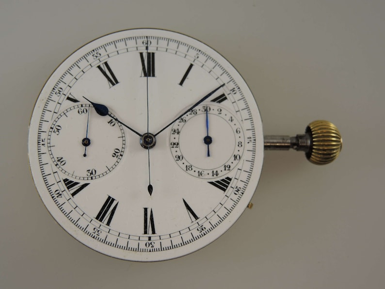 May include: A white chronograph pocket watch with black Roman numeral hour markers and black hands. The watch has two sub-dials, one for seconds and one for minutes. The watch is attached to a winding key.