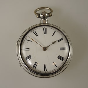 May include: A silver pocket watch with Roman numeral hour markers and a white face. The watch has a silver chain attached to the top.