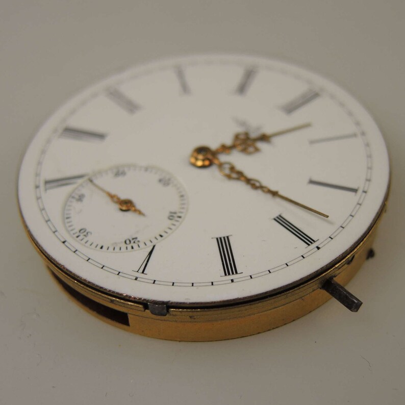 May include: A gold pocket watch with a white face and black Roman numeral hour markers. The watch has a smaller sub-dial for seconds.