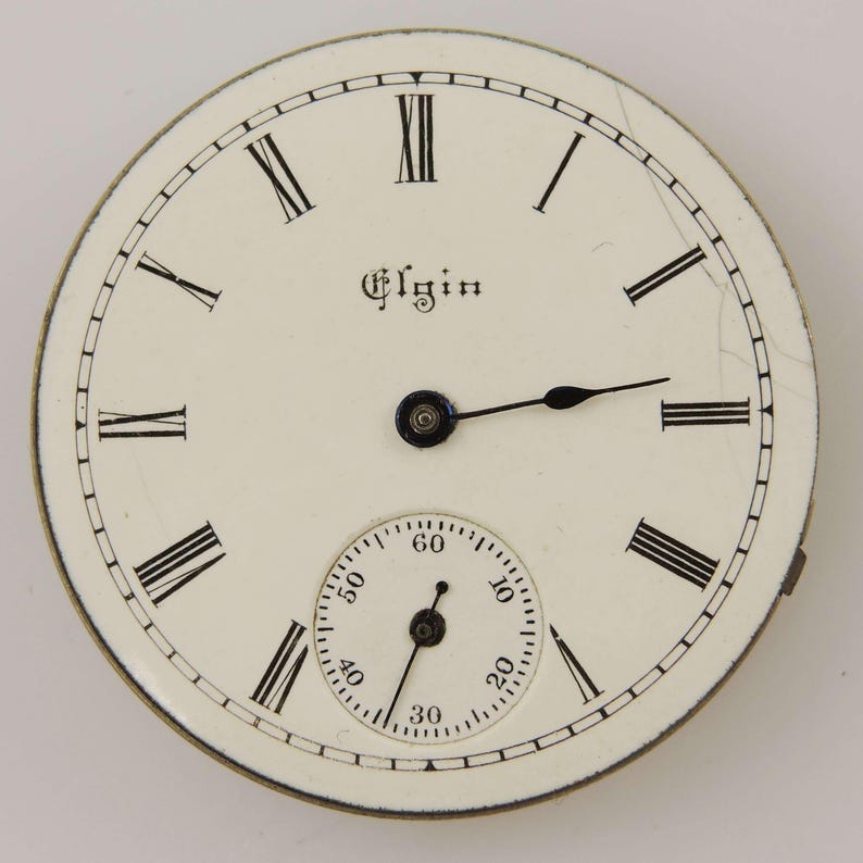 May include: Antique Elgin pocket watch face with a cream-colored background. Black Roman numerals mark the hours, with a smaller seconds dial at the bottom. The word "Elgin" is printed in a decorative font. Black hands indicate the time.
