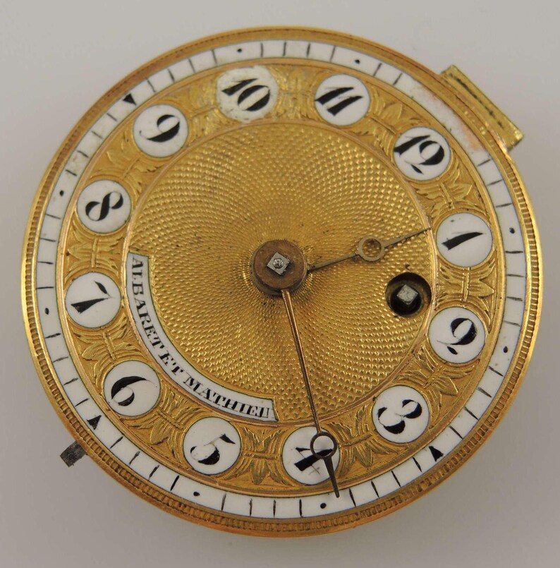 Puede incluir: Una esfera de reloj de bolsillo de oro con marcadores de hora en n&uacute;meros romanos y una esfera de esmalte blanco. La esfera del reloj est&aacute; grabada con un dise&ntilde;o floral y el texto "ALBARET ET MATHIEU".