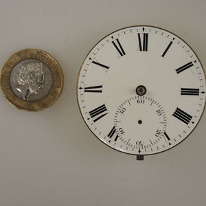 Puede incluir: Una esfera de reloj blanca con n&uacute;meros romanos negros para las horas y marcas negras para los minutos. La esfera est&aacute; rodeada por un borde plateado.