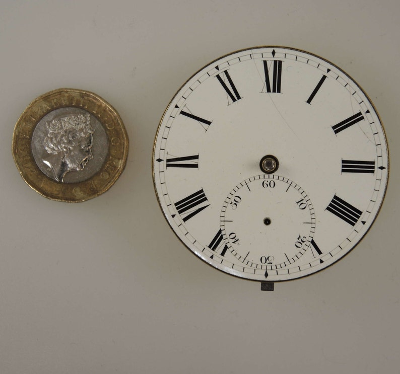 Puede incluir: Una esfera de reloj blanca con n&uacute;meros romanos negros para las horas y marcas negras para los minutos. La esfera est&aacute; rodeada por un borde plateado.