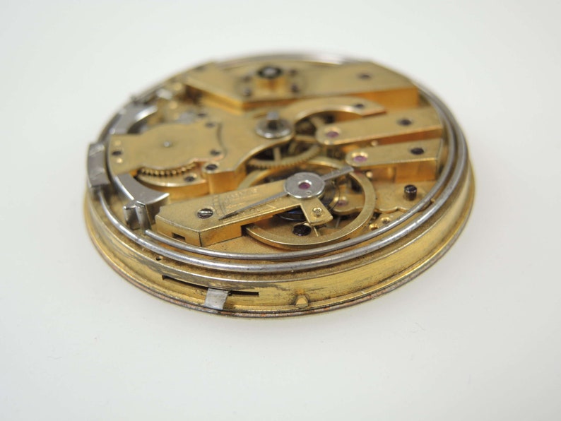 Op de afbeelding: Close-up van een goudkleurig zakhorlogemechanisme met ingewikkelde tandwielen en een zilverkleurige buitenring.
