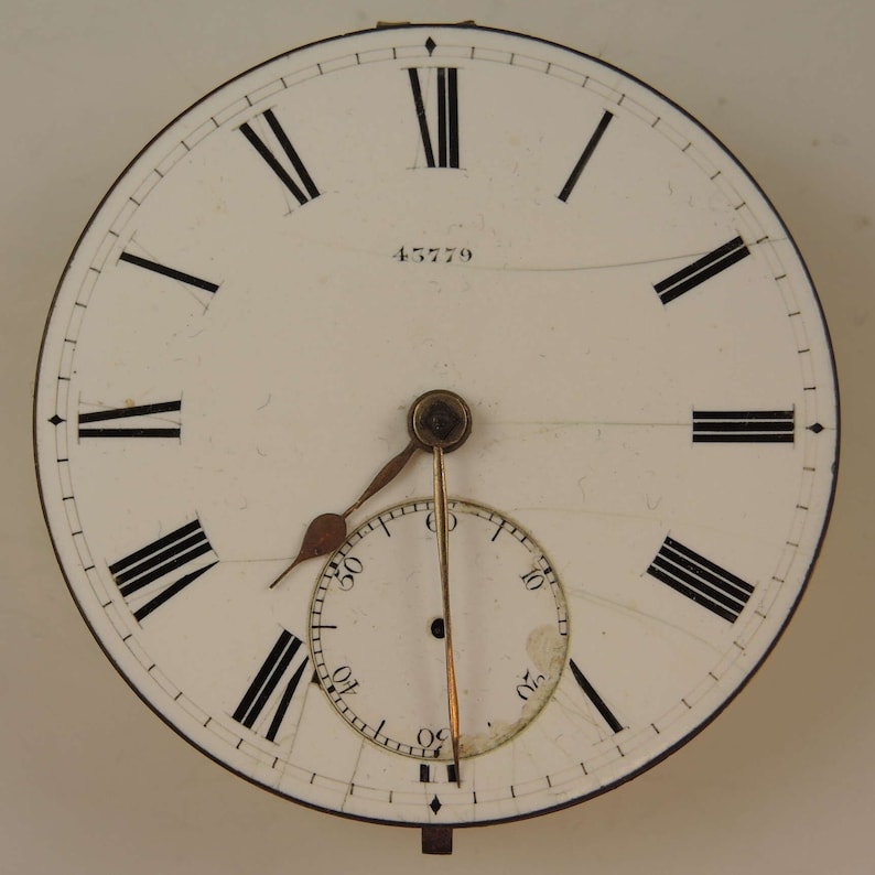 May include: White clock face with black Roman numeral hour markers and black minute markers. The clock face has a small, white sub-dial with black markings. The clock face has the number 45779 printed on it.