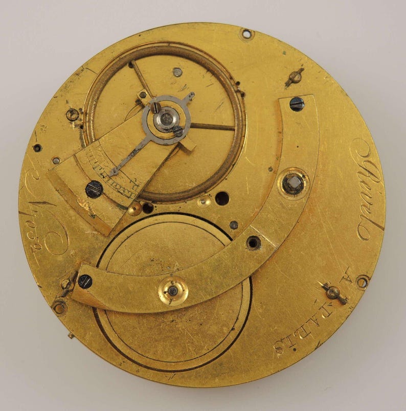 May include: Close-up of a gold-colored pocket watch movement with intricate gears and a lever. The watch is labeled "A.L. Adams" and "Geneva" on the back.