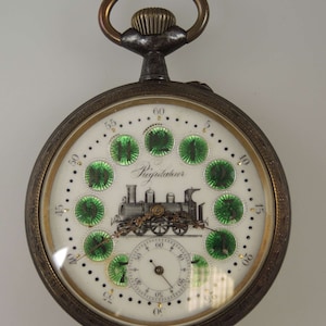 May include: A silver pocket watch with a white face and green accents. The watch features a train engine design and the text "Regulateur" on the face.
