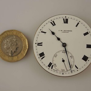 Puede incluir: Una esfera de reloj de bolsillo blanca con marcadores de hora en n&uacute;meros romanos negros y agujas negras. La esfera del reloj tiene un anillo exterior negro con marcas para segundos y minutos. La esfera del reloj tambi&eacute;n tiene el texto "J.W. BENSON LONDON" impreso en ella.